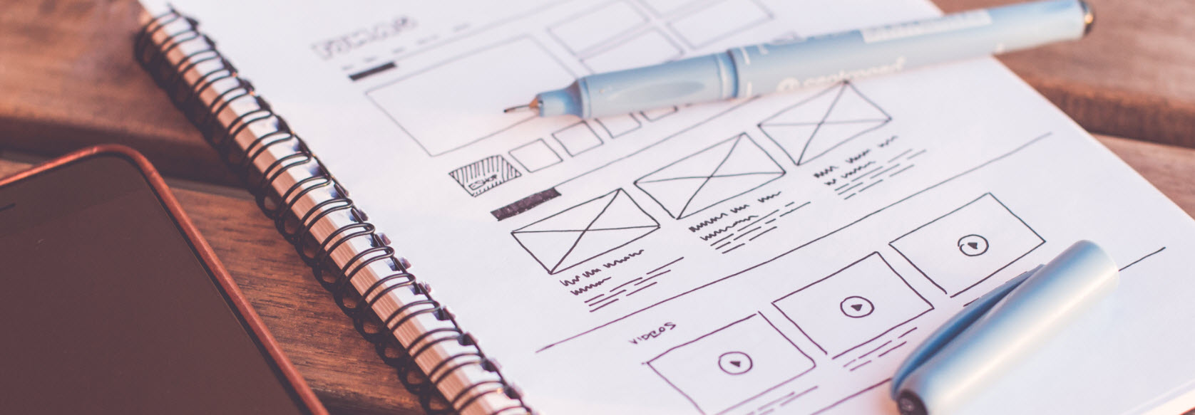 Hand-drawn wireframe of a website on a notebook with a pen